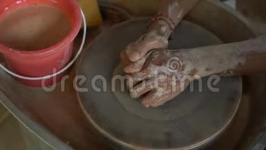一个教师陶工教他的徒弟如何在陶工的轮子上做一个泥碗的慢速特写镜头`